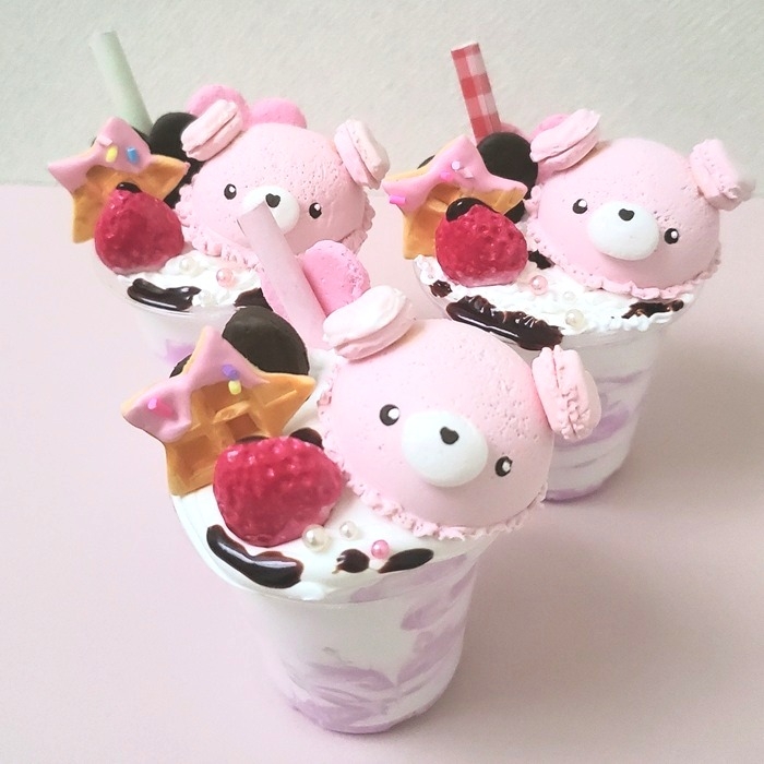 ピンクの天使マカロンがのったデコレーションスイーツ作品。ピンクの羽と耳が可愛いマカロンを透明カップに盛りつけた写真。