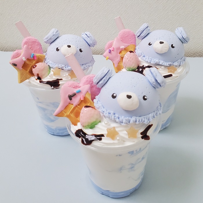 天使の羽をつけた白いマカロンがのったデコレーションスイーツ。透明カップに盛りつけられた可愛いエンジェルマカロンの作品。